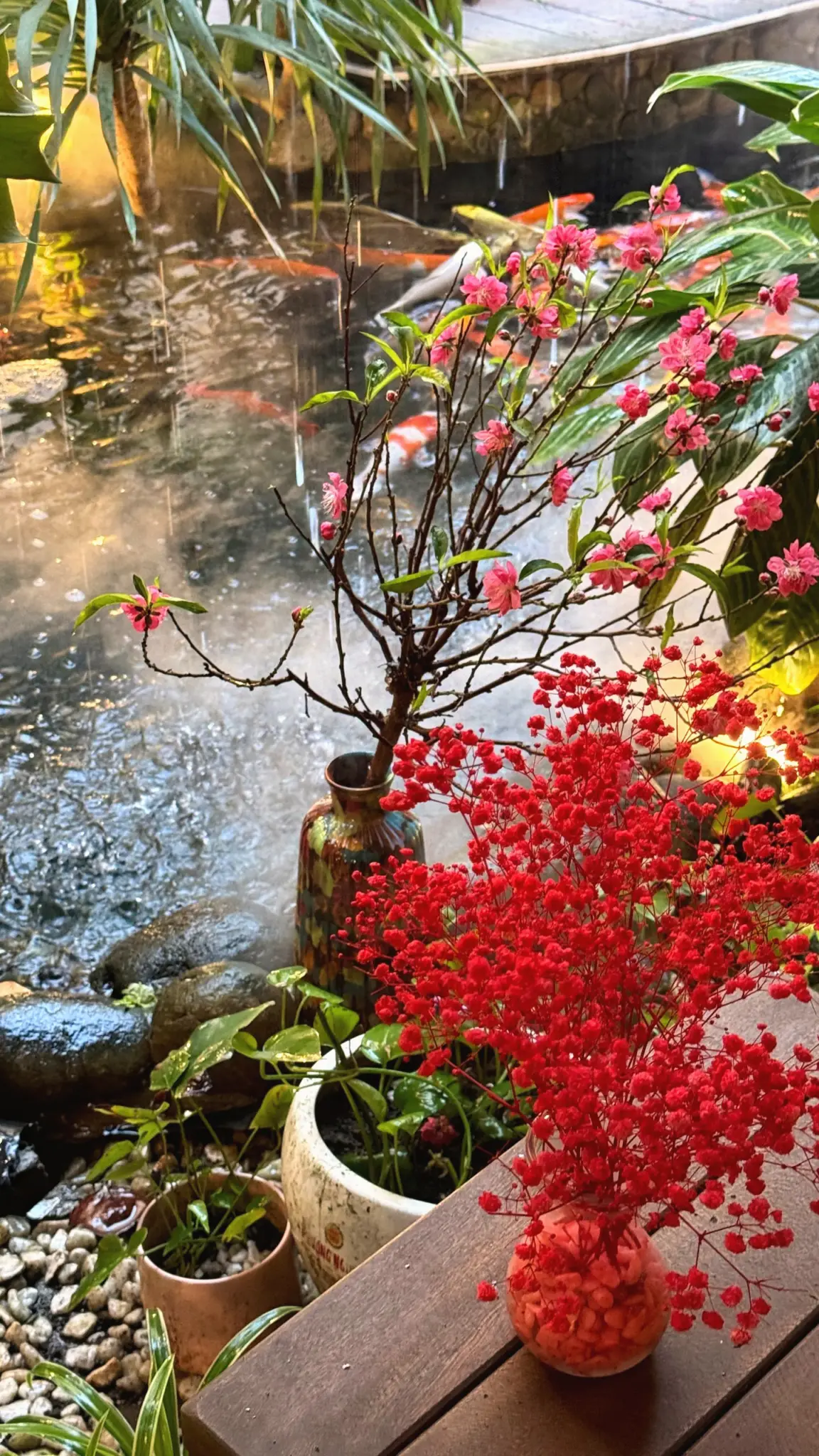 Vases of red blossom on a wooden ledge beside a koi pond