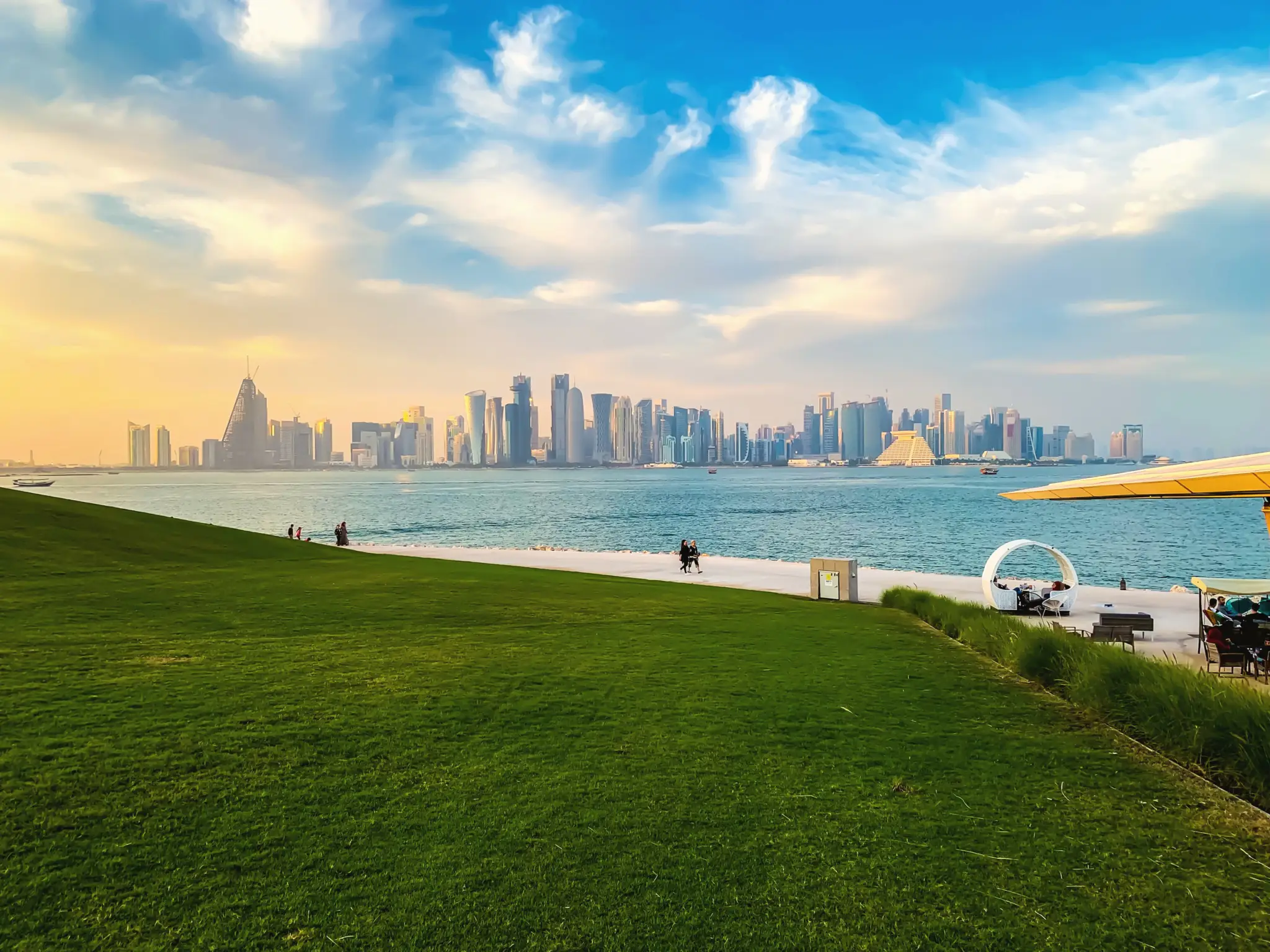 Doha skyline across the bay from the green lawn of MIA Park under a wide blue sky
