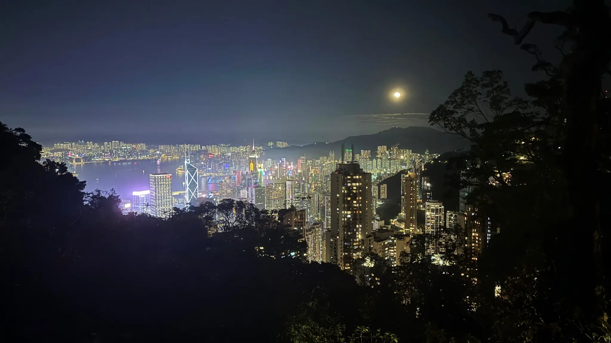 Moon rising over Victoria Harbour and the lit skyline seen from the hills
