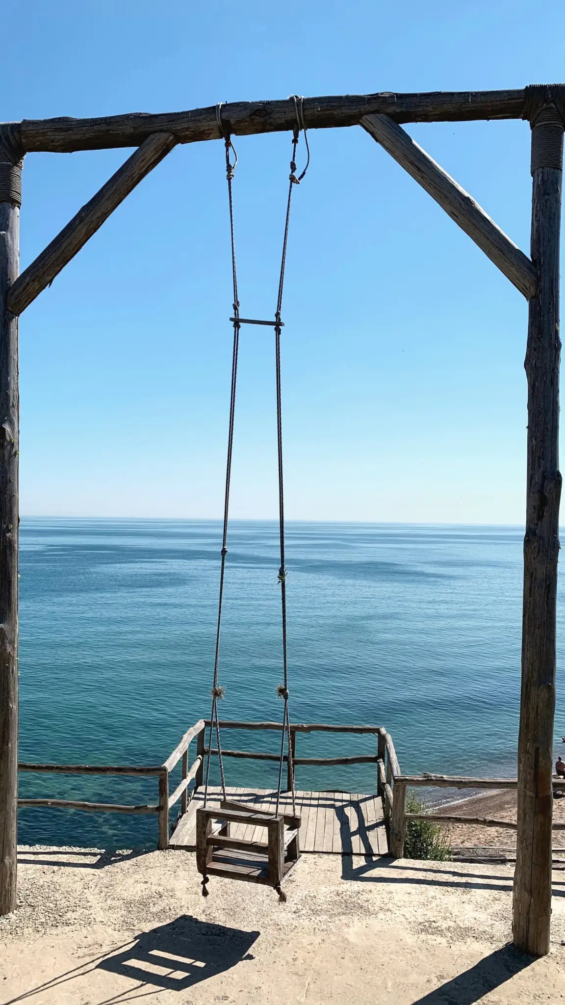 Wooden swing hanging from a timber frame above the blue sea