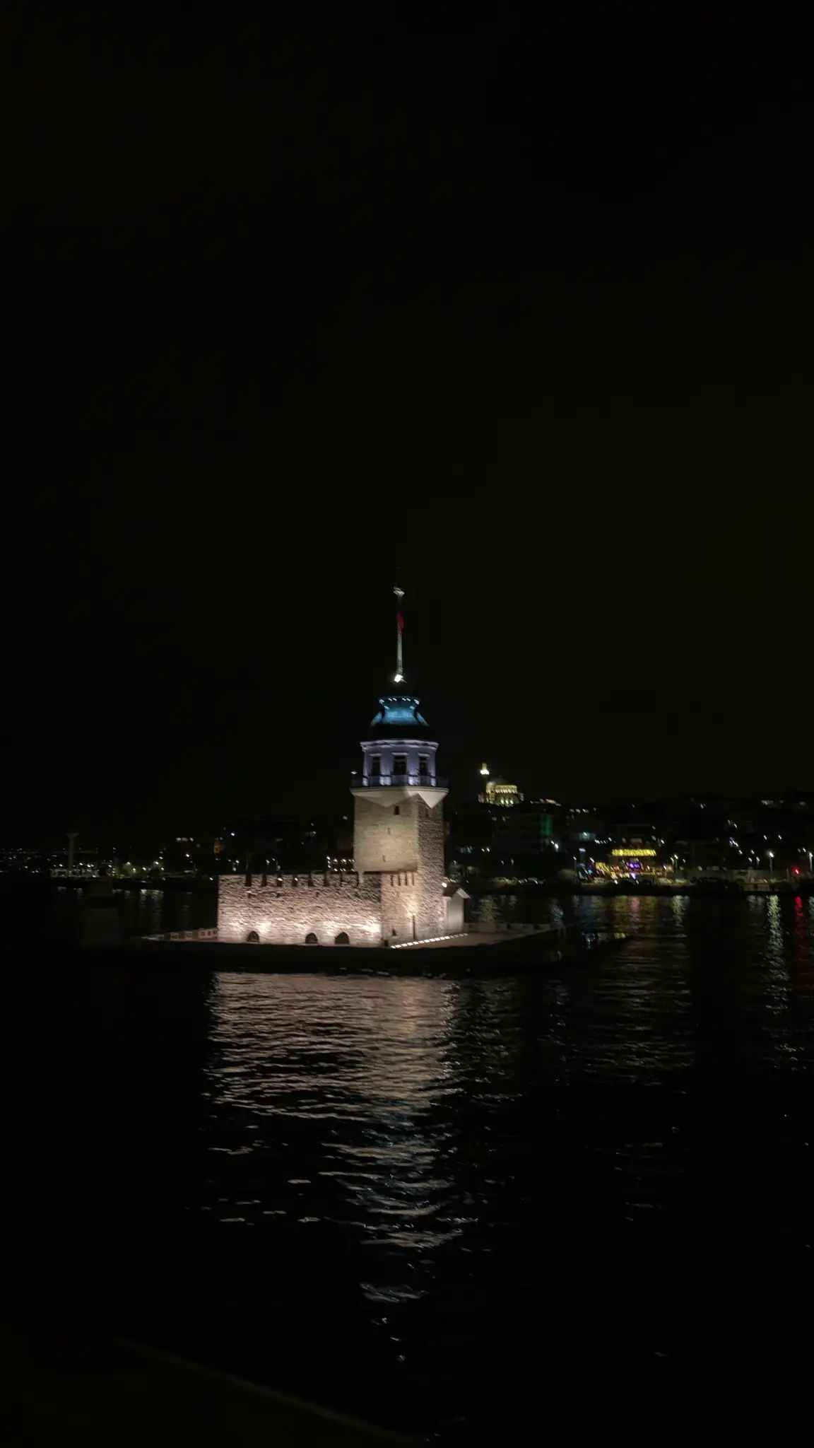 Maiden's Tower lit up at night, reflected in the dark water