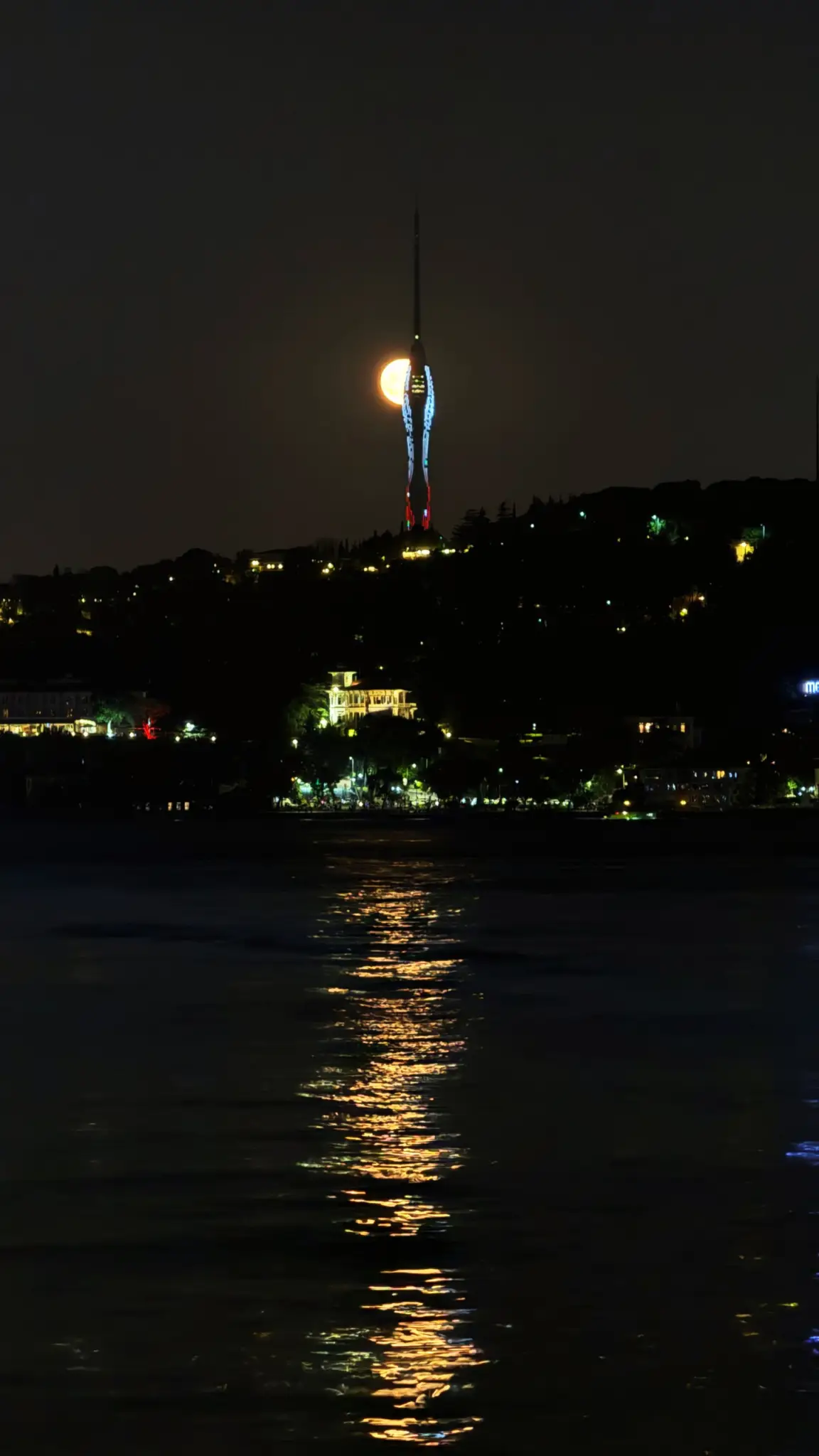 Full moon beside the lit Çamlıca TV tower, reflected in the Bosphorus at night