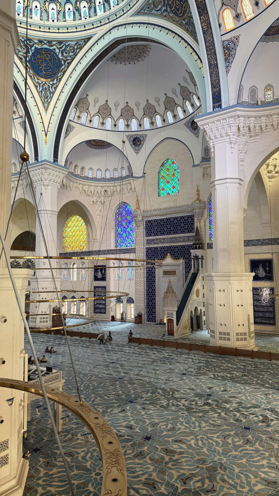 Vast mosque interior with stained-glass windows and patterned blue carpet