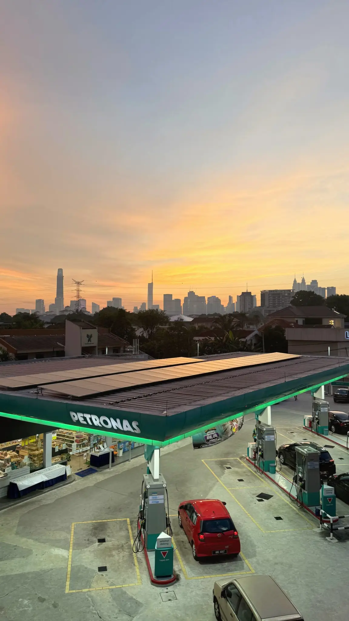 Petrol station forecourt below a distant city skyline at sunset