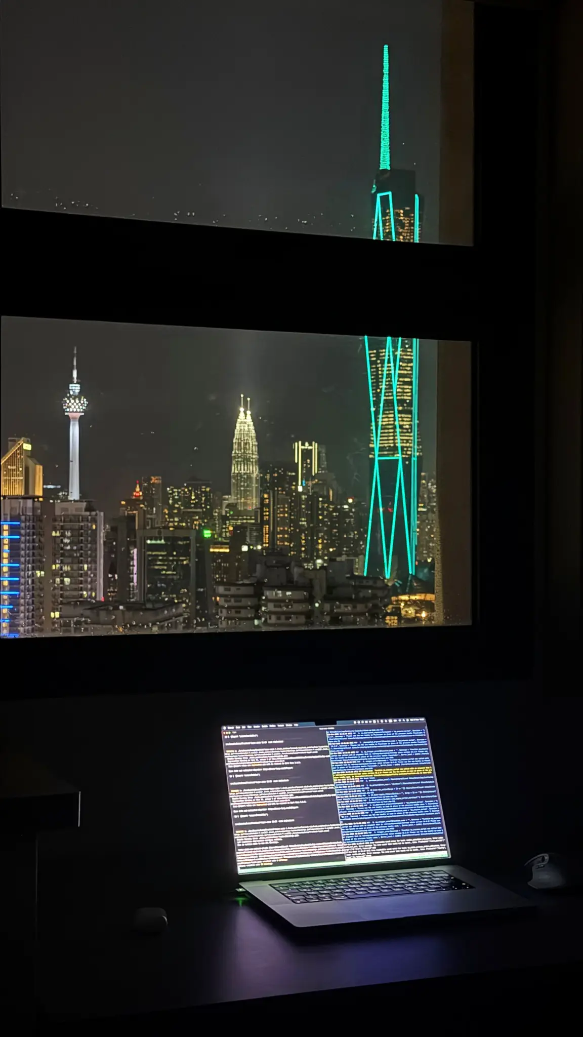 Laptop on a desk by a window overlooking the lit Kuala Lumpur skyline