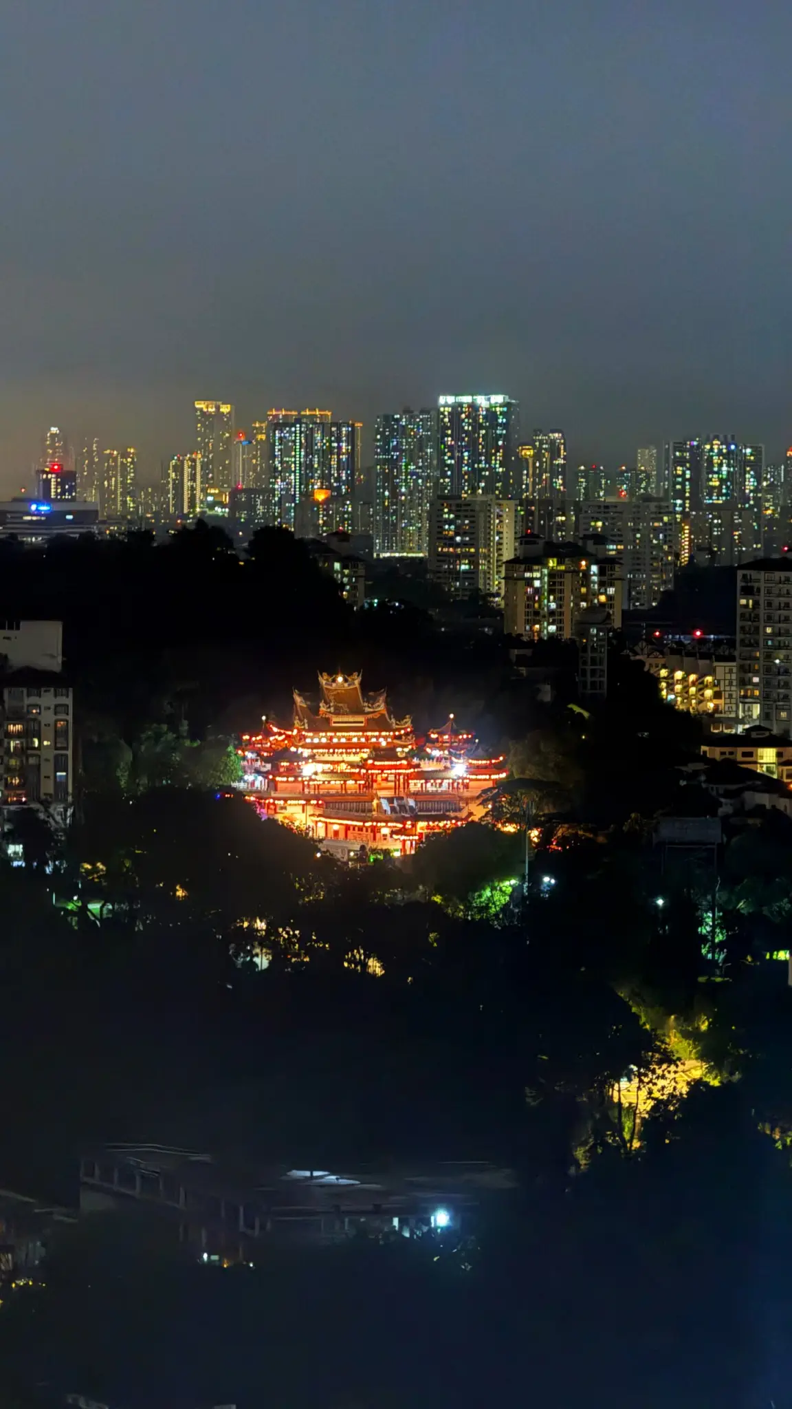 Glowing Chinese temple on a hill against the city skyline at night
