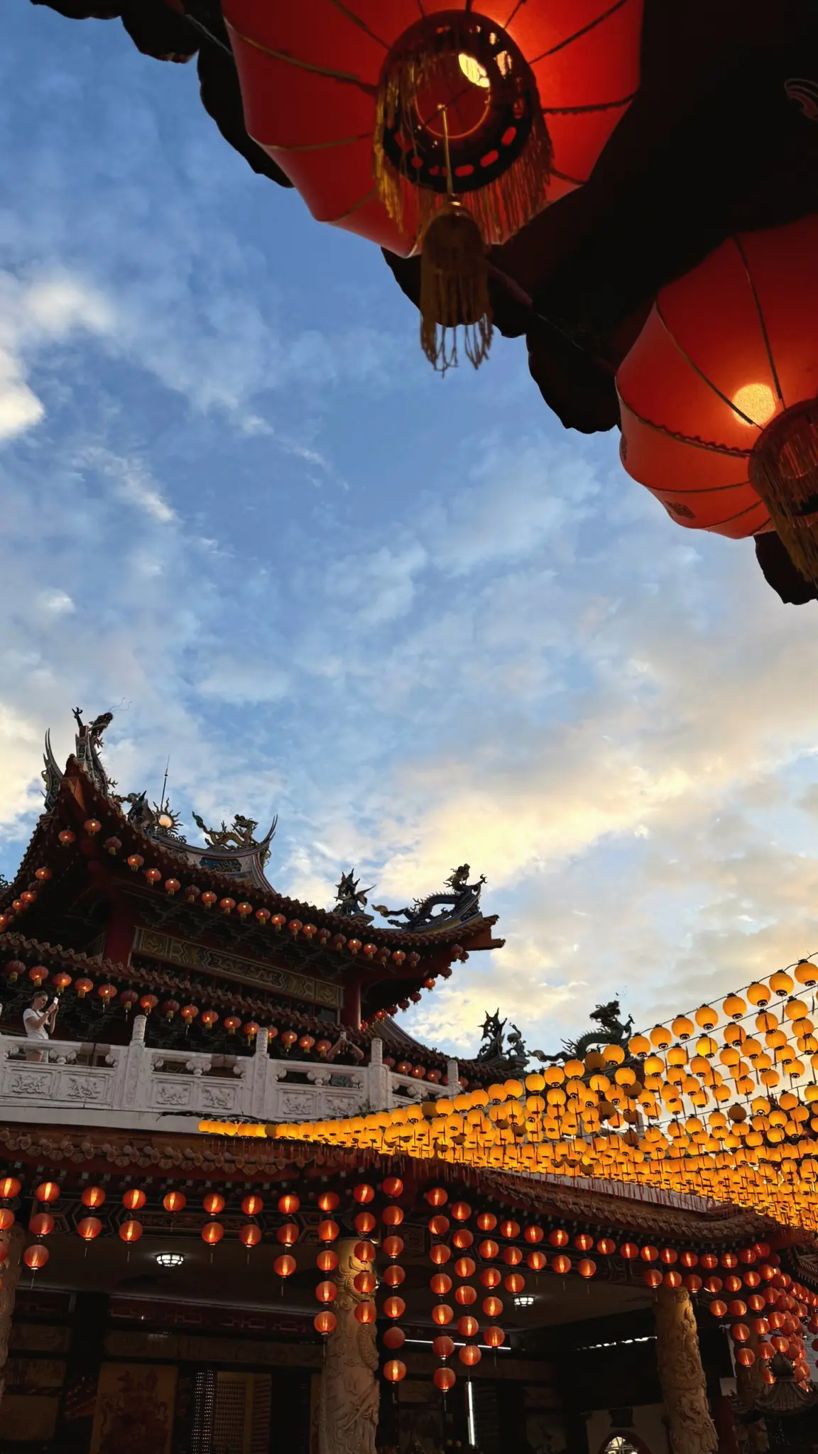 Chinese temple roof under rows of glowing red lanterns at dusk