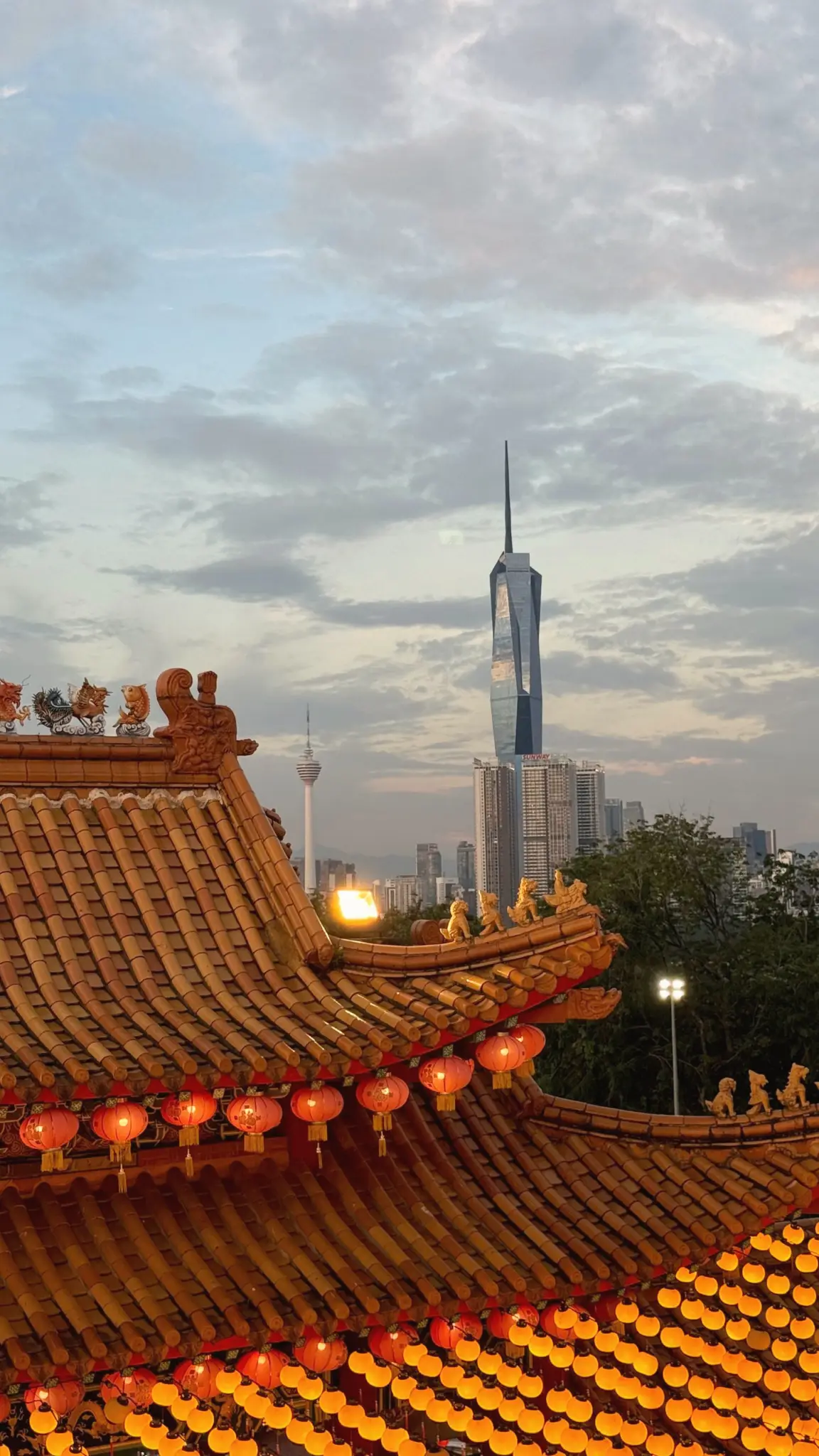 Lantern-strung temple rooftops with Merdeka 118 rising behind at dusk