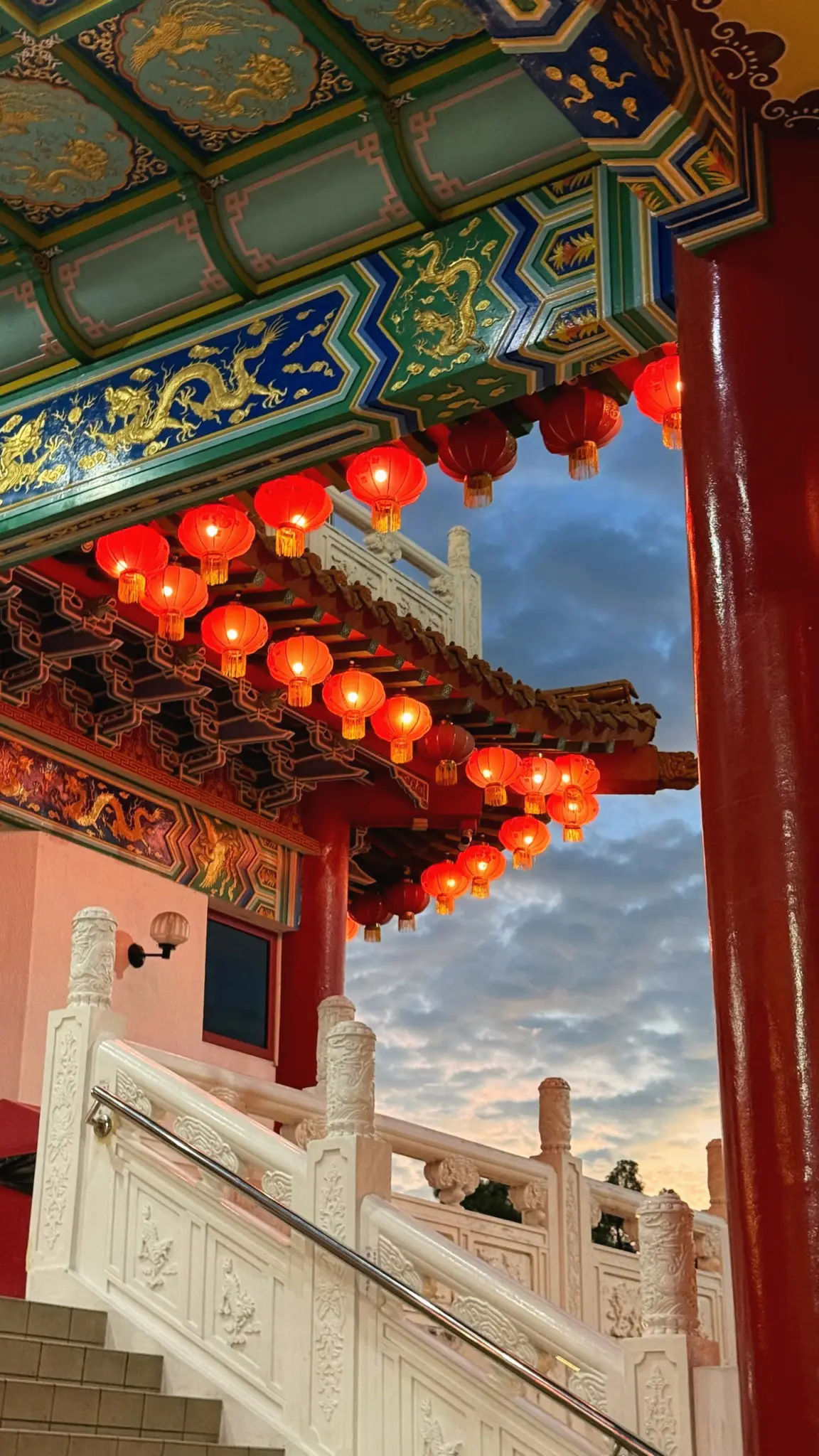 Red lanterns hanging from a painted temple eave above white stone stairs