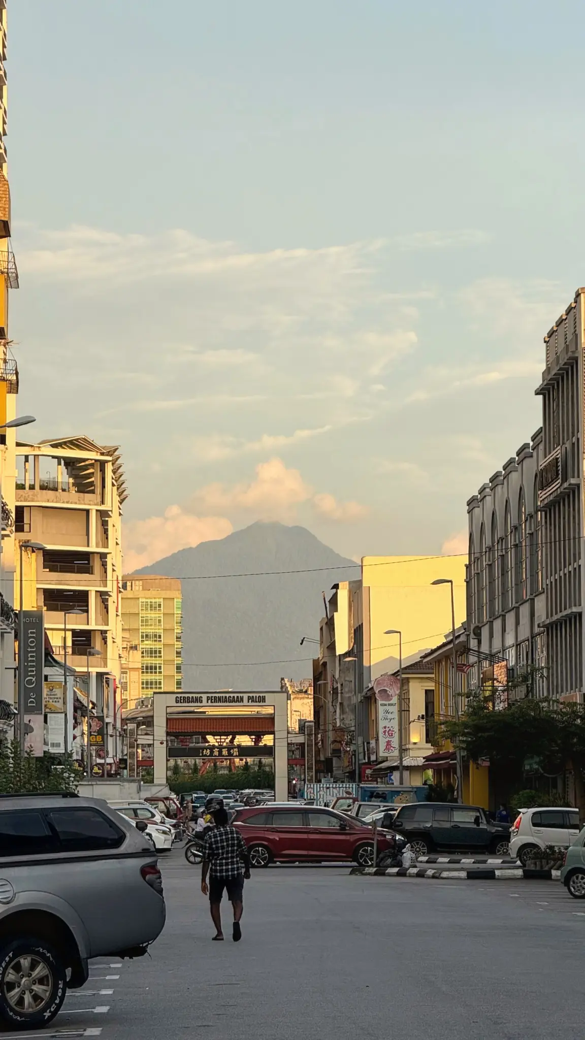 Man walking down a city street towards a mountain in golden evening light