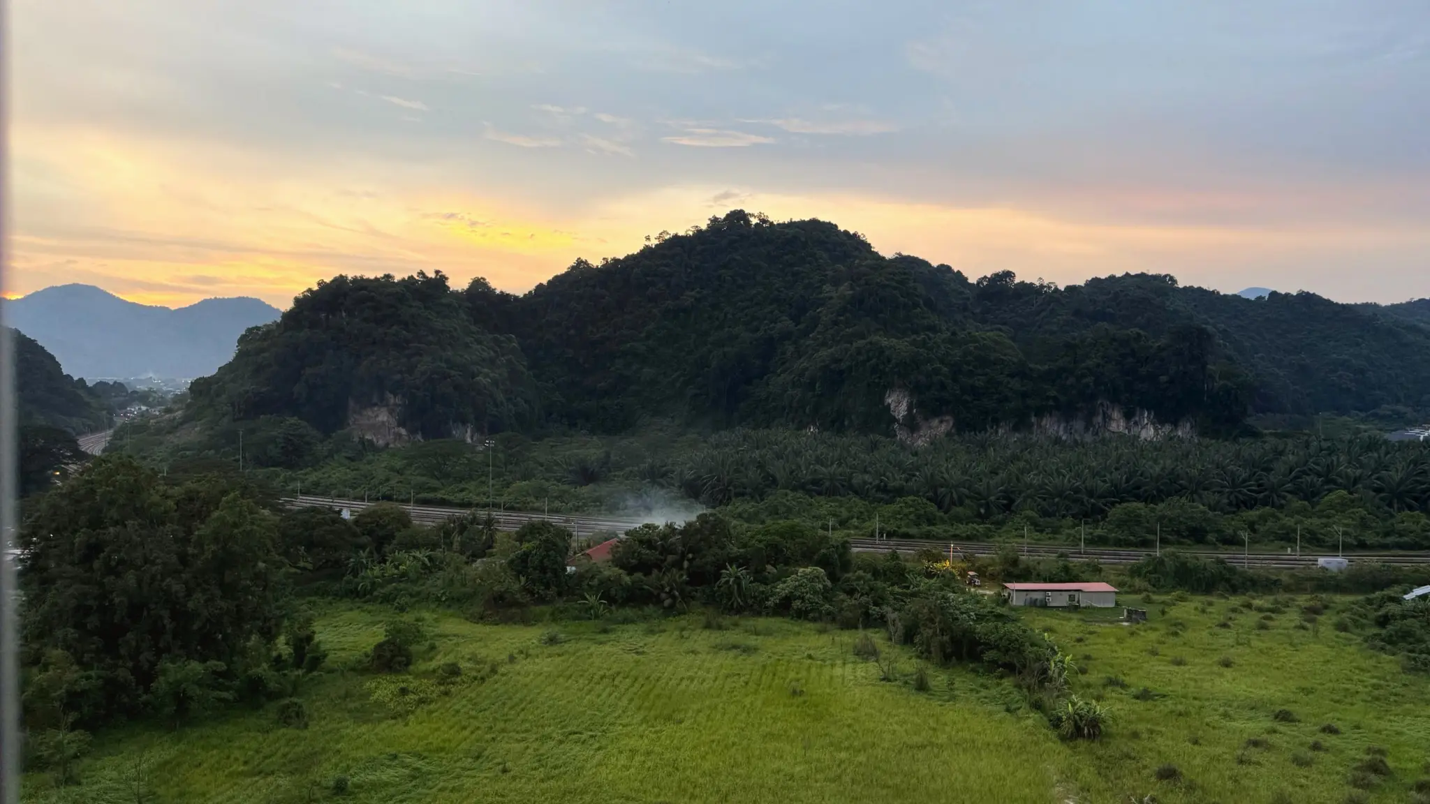 Sunset over forested limestone hills and green fields seen from above