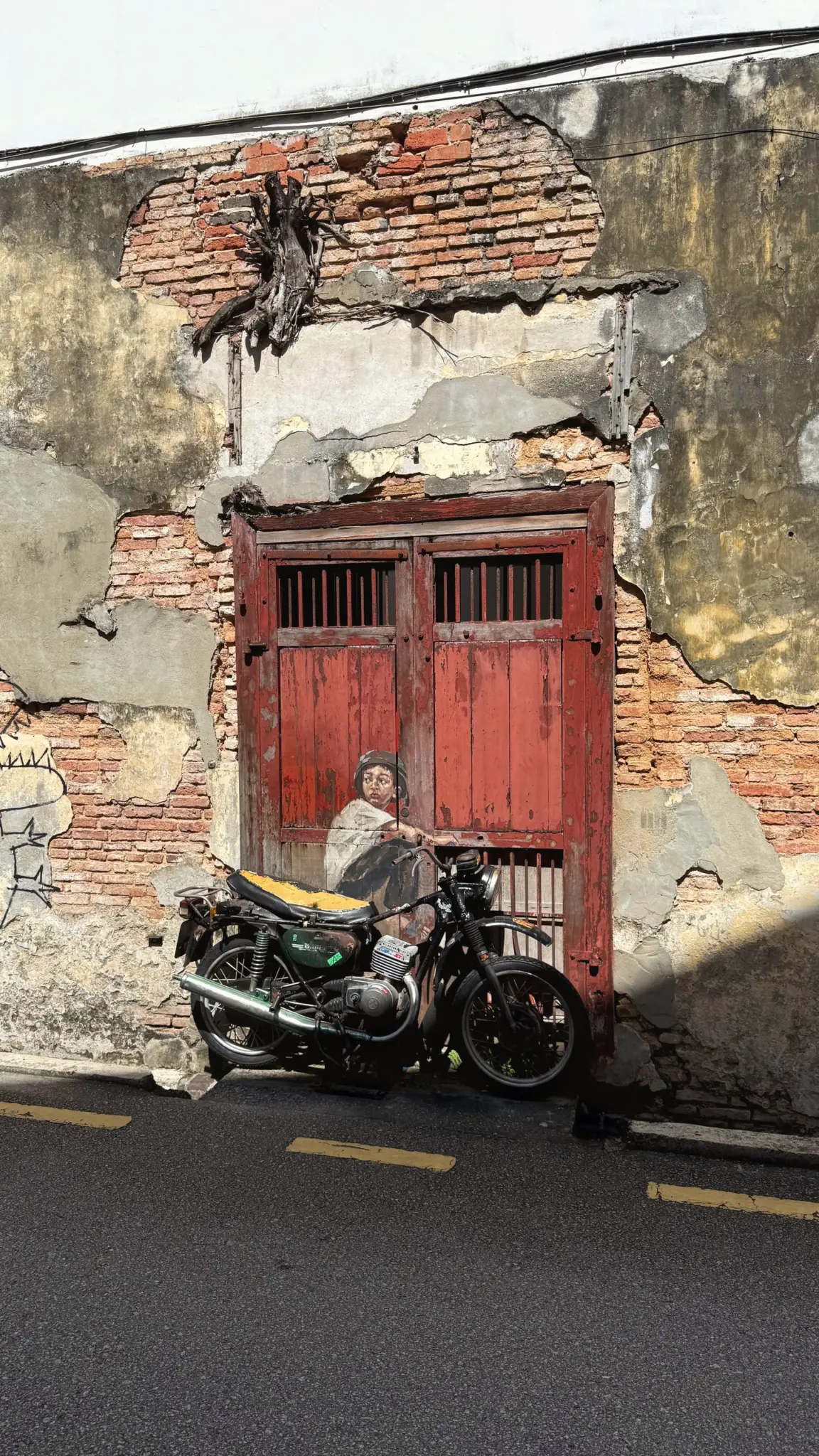 Street mural of a boy on a real vintage motorbike by a red door