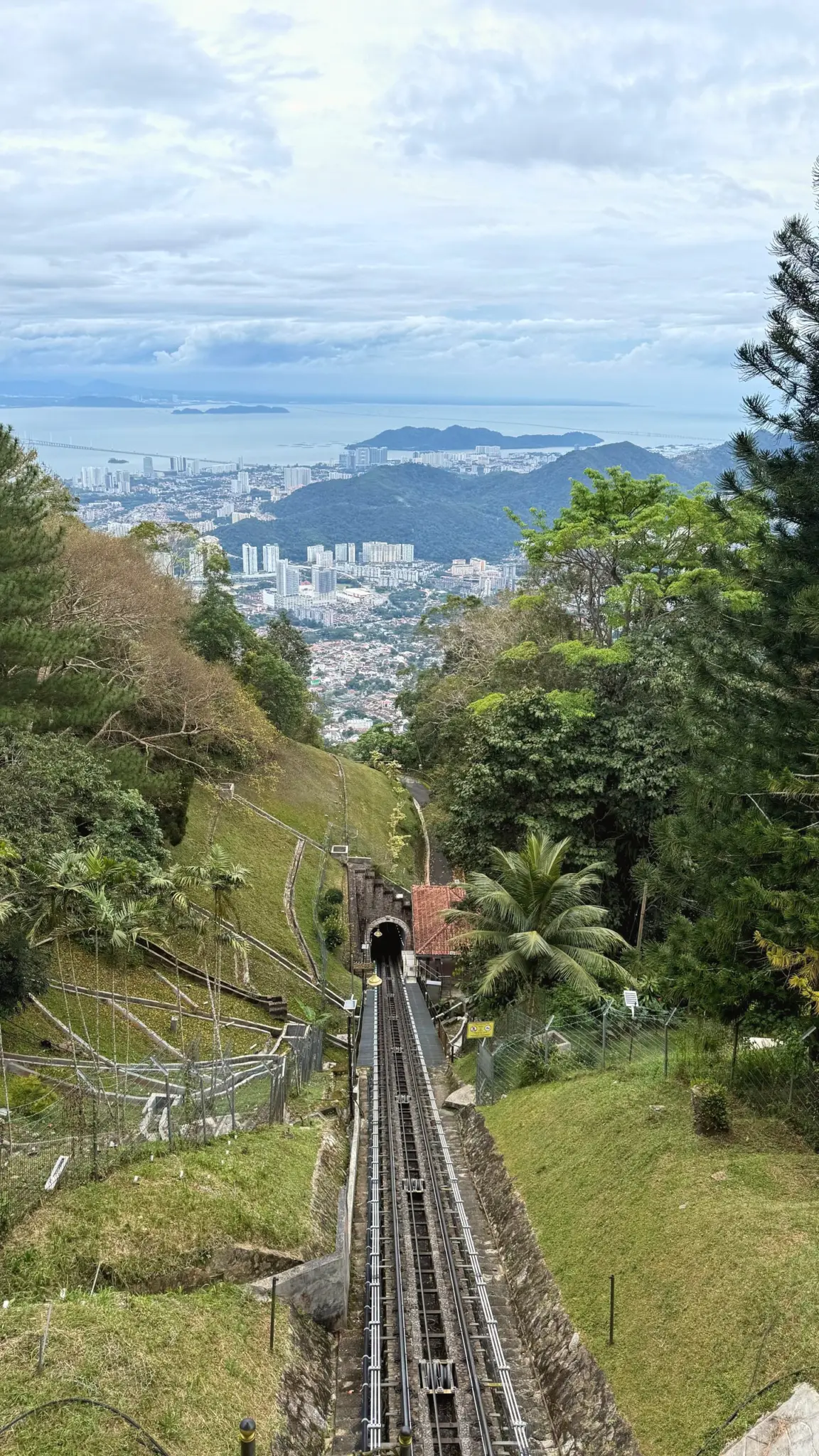 Funicular track descending a green hillside towards the city and sea