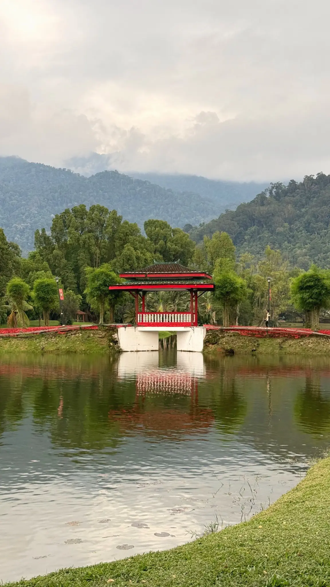 Red and white pavilion bridge reflected in a lake beneath misty hills