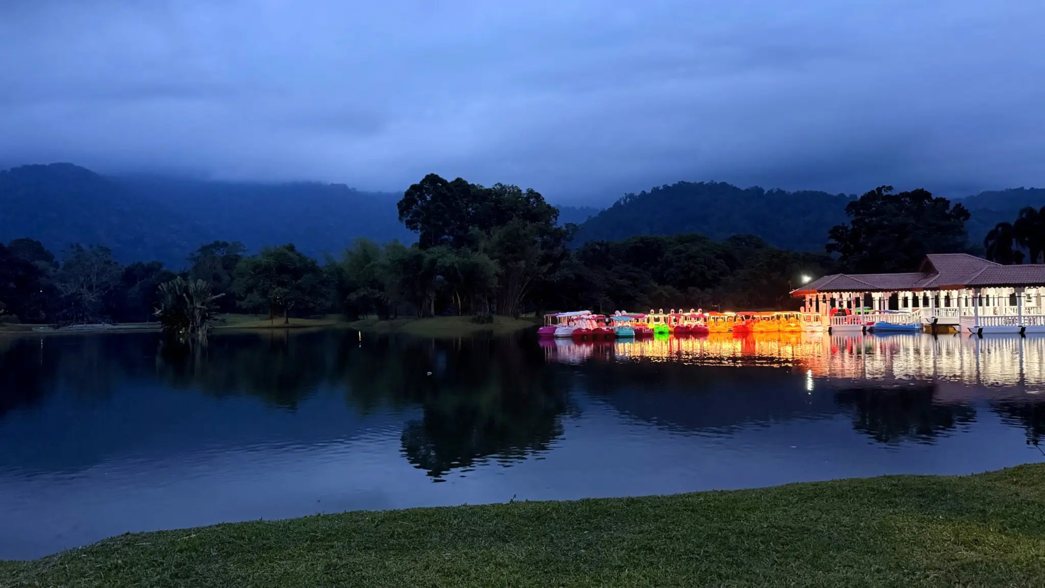 Lit boathouse and pedal boats on a still lake at dusk